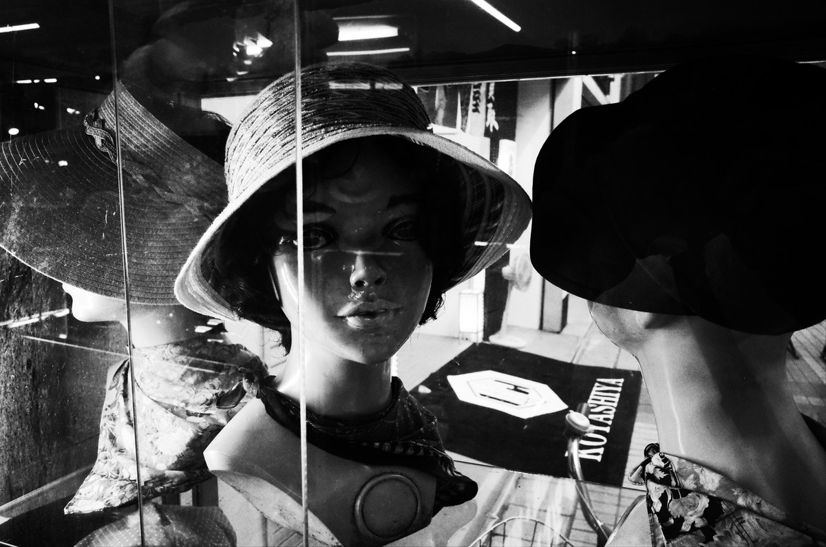 ガラス越しに重なり合う帽子姿のマネキン