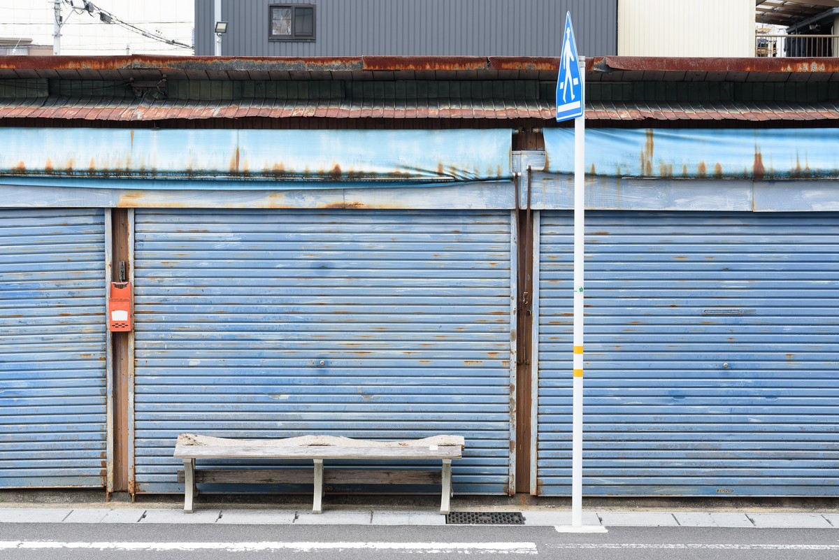 青いシャッターの前に置かれた使い込まれたベンチ